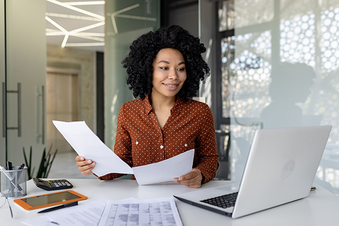 Young successful financier works with documents and contracts inside the office, satisfied with the results of financial activities, businesswoman reviews accounts, reports and contracts, laptop.