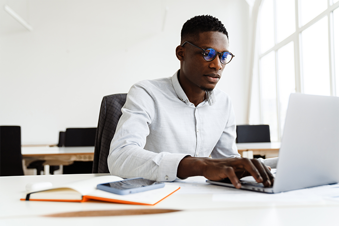 African-American man in eyeglasses working with laptop while sitting in office