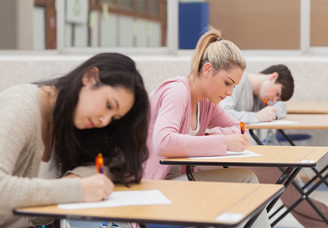 Students taking exam in classroom. Education test and literacy concept. Cropped shot, hand detail.