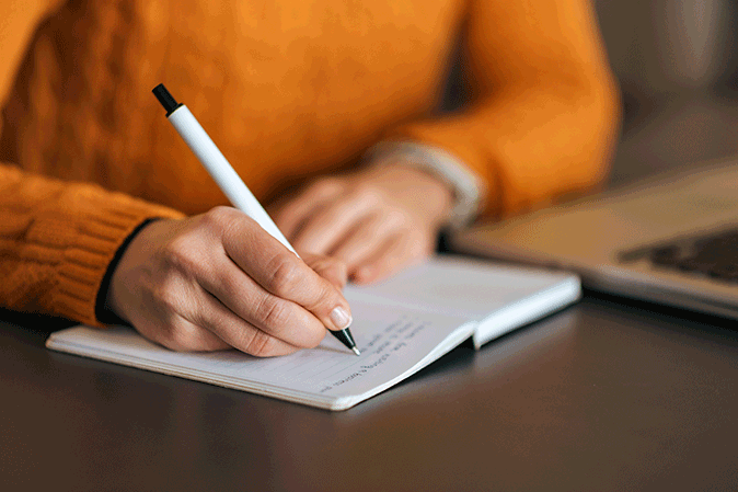 Person writing notes in a notebook while sitting at a table