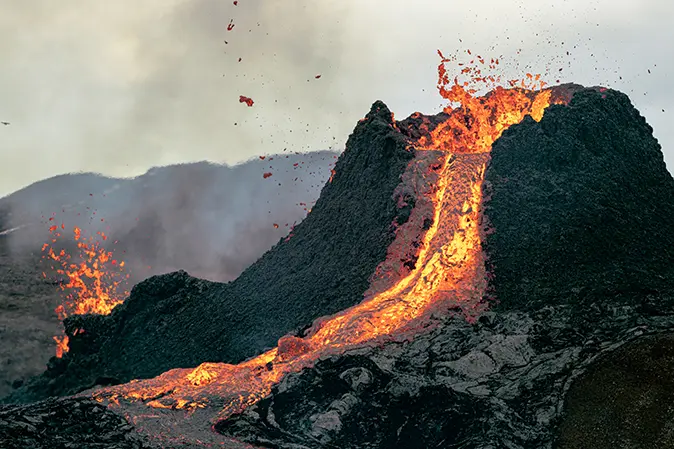 Hot lava flowing out of the peak of a small mountain