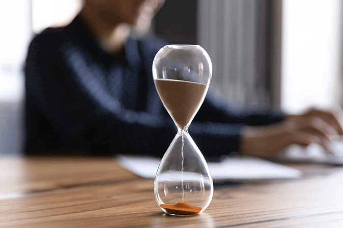 Hourglass on a desk in front a woman working on computer