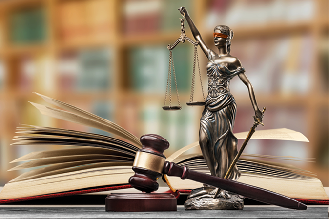 Lady of justice holding scales between a judge's gavel and a book in a library
