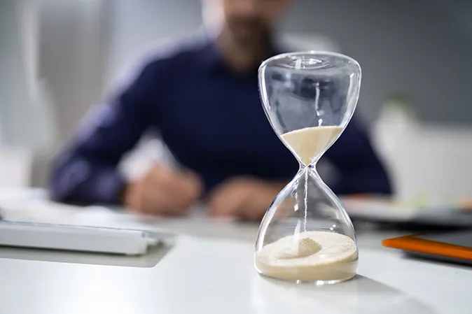 Man sitting at a desk behind an hour glass that's running out of sand
