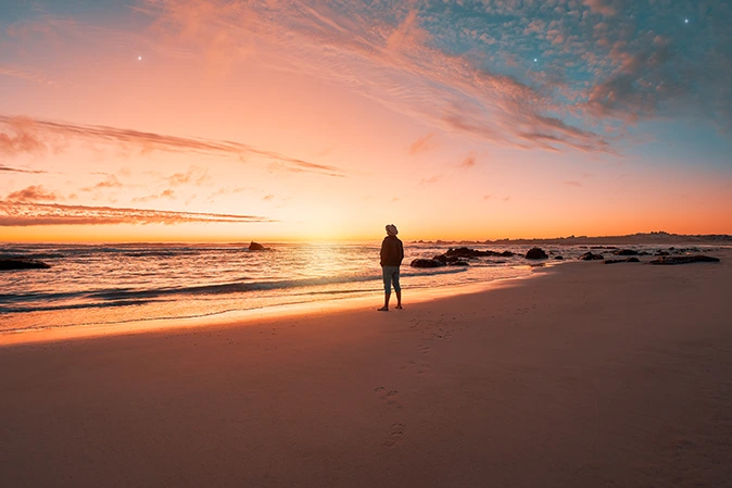Man standing on the beach looking out to the ocean at sunset