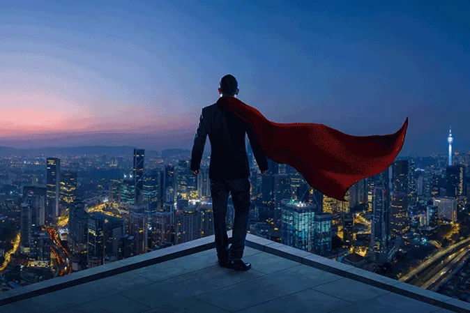 Business man wearing a cape overlooking a city at night
