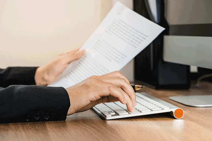Man looking at a letter while typing on a laptop