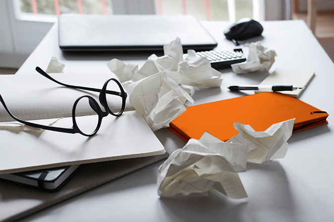 Messy desk with pair of glasses and crumpled papers and notebooks