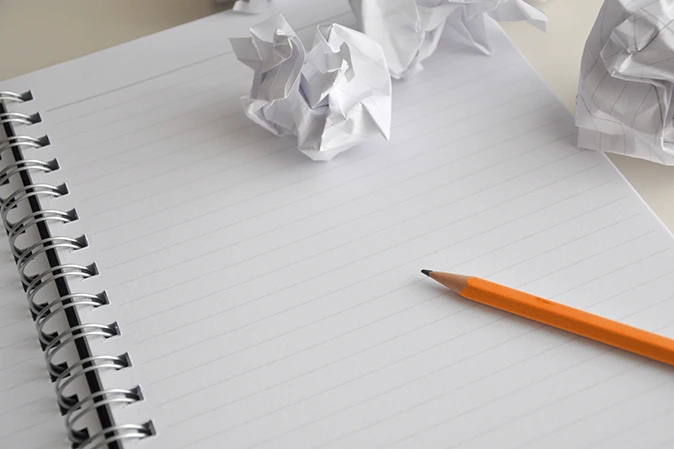 Notebook and pencil with a couple crumpled pages around them