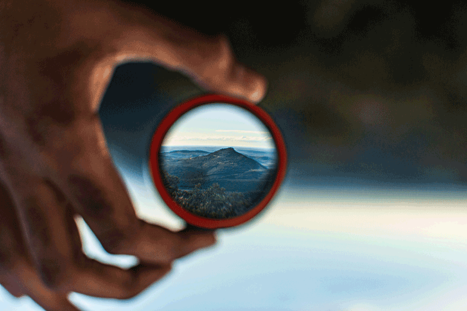 Person holding a glass with the view of the mountains in it