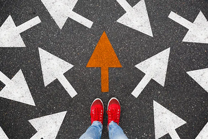 Person with red sneakers surrounded by arrows pointing in different directions on the pavement