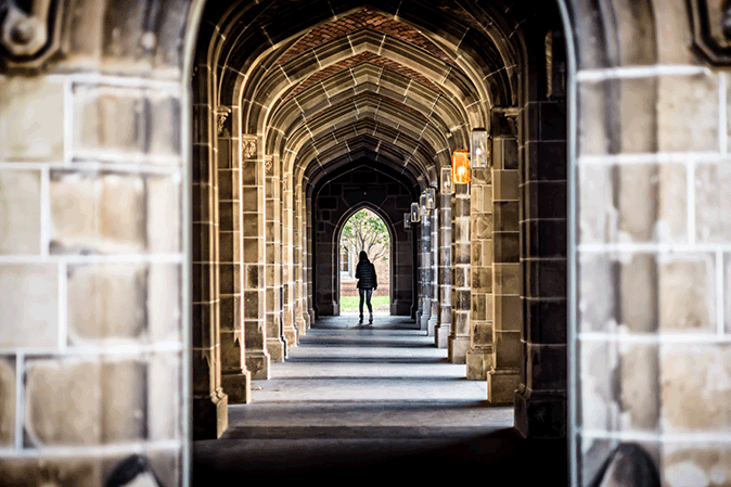 Long stone arch hallway at a university with a woman in the distance