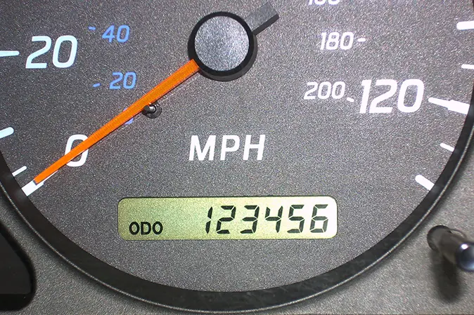 View of a car's odometer with an orange needle showing mileage