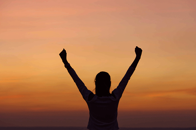 Woman with arms up in victory at sunset