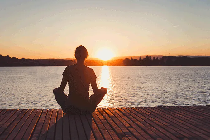 Woman meditating while sitting on a dock by a lake