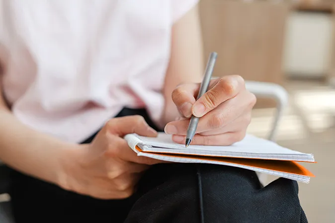 Woman taking notes in a pad sitting on her lap