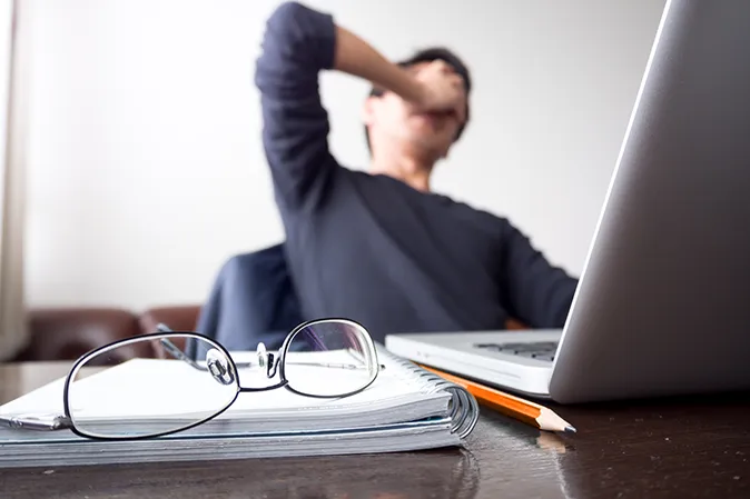 Young man sitting in front of his laptop with hands over his eyes in frustration
