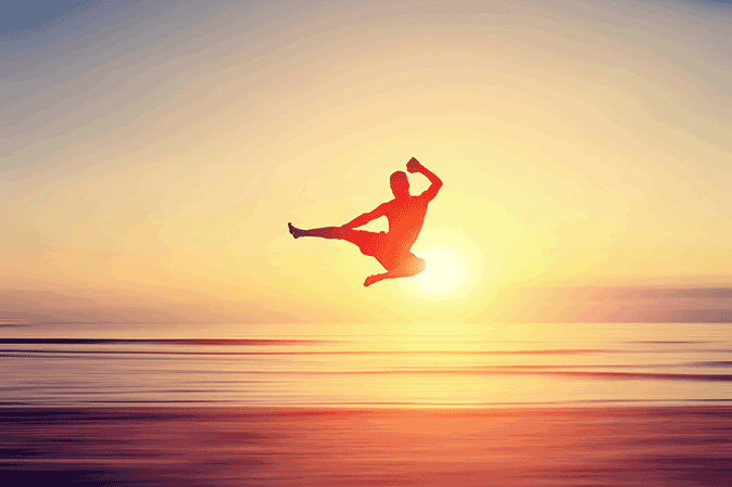 Young man on the beach performing a karate kick at sunset