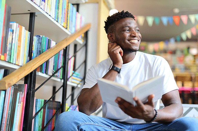 Young man smiling while sitting on steps in library with a book
