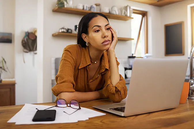 Young woman with her head in her hand looking bored at her laptop 