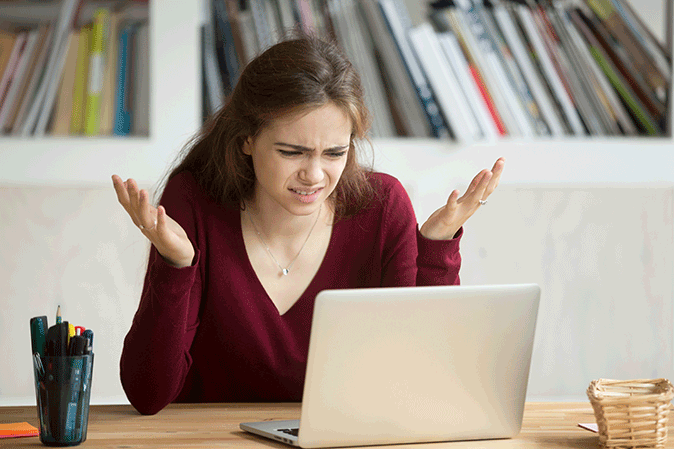 Young woman looking at her computer in confusion with hands up in frustration