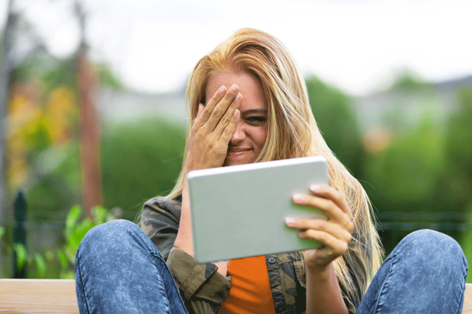 Young woman covering her eyes while peeking at her tablet