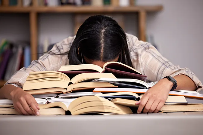 Young woman face down on top of a pile of books