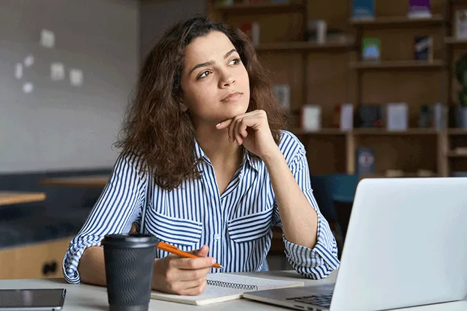Young woman in thought writing notes in front of a laptop