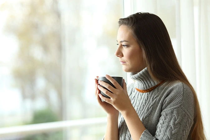 Young woman holding a coffee mug looking out a window
