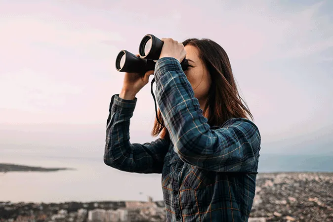 Young woman looking through binoculars by a body of water