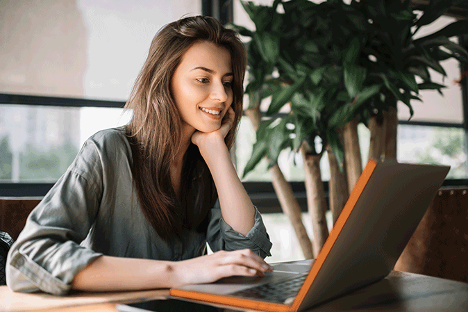 Young woman with chin in her hand smiling at her laptop