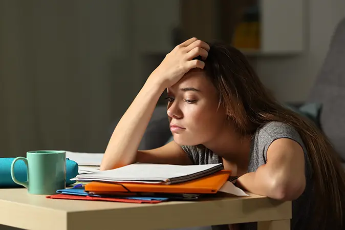 Young woman looking tired staring at school notebook