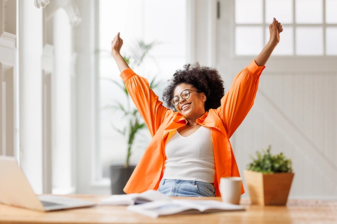 Young woman at home in front of laptop stretching arms in victory