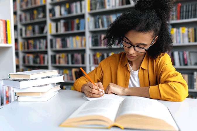 Young woman writing notes while reading a book in a library