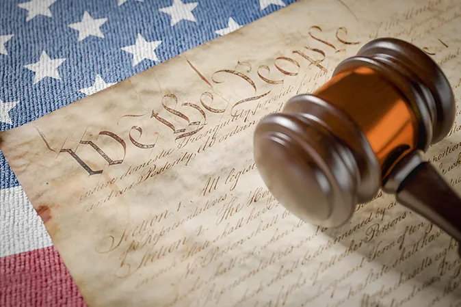 Judge's gavel sitting on the US Constitution with the American flag in the background