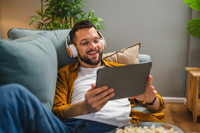 Young man wearing headphones sitting on a couch on his tablet