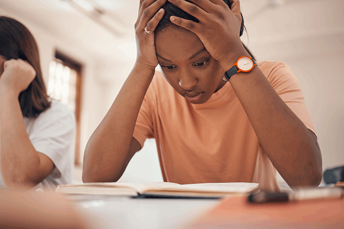 Young woman holding her head in frustation sitting at her desk in class