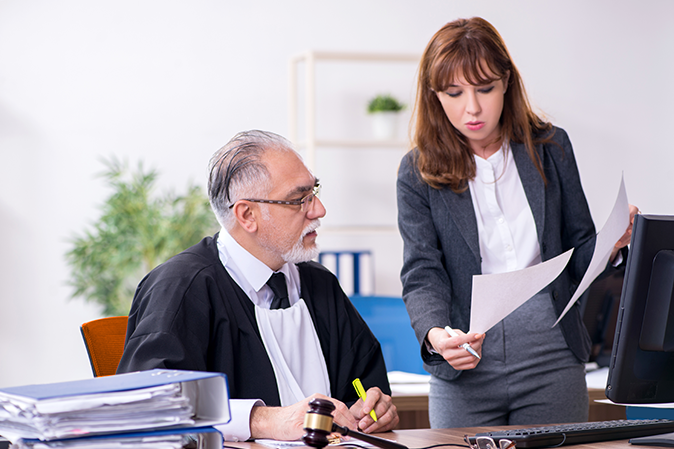 Judge sitting at his desk with a young woman assistant standing next to him showing documents