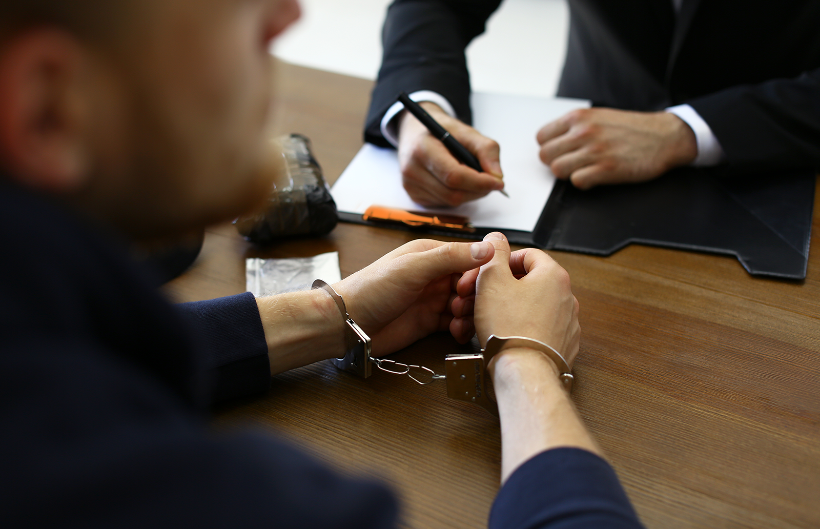 Man in handcuffs sitting before a lawyer who is taking notes