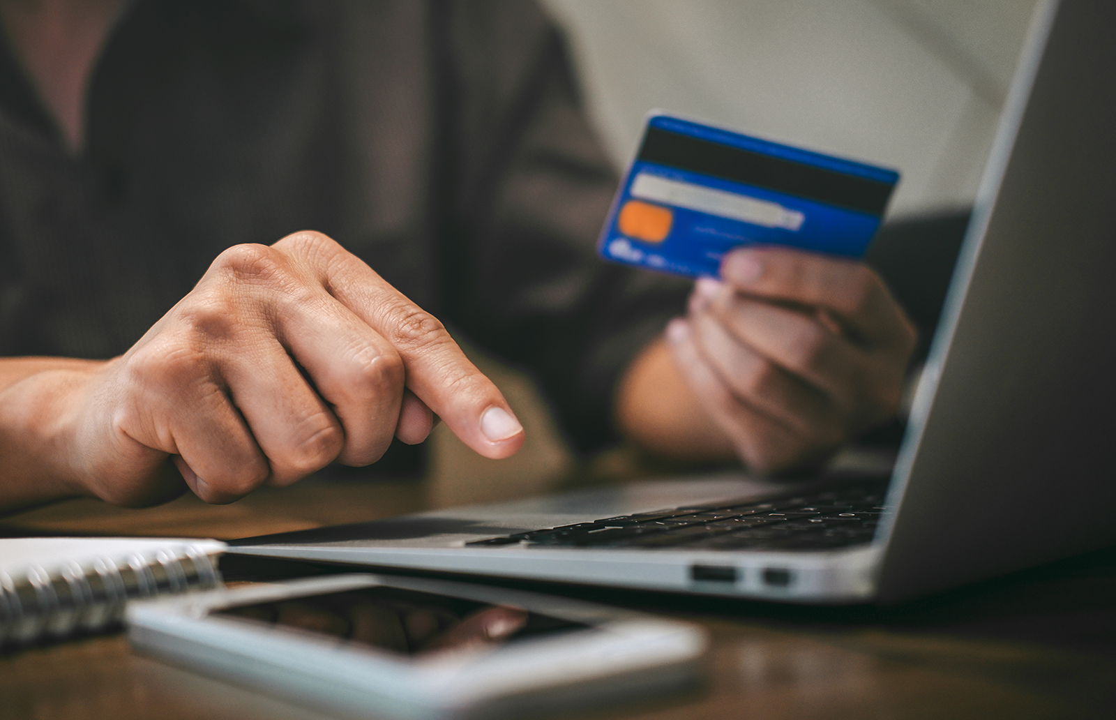 Person holding a credit card while typing on a laptop with a mobile device nearby