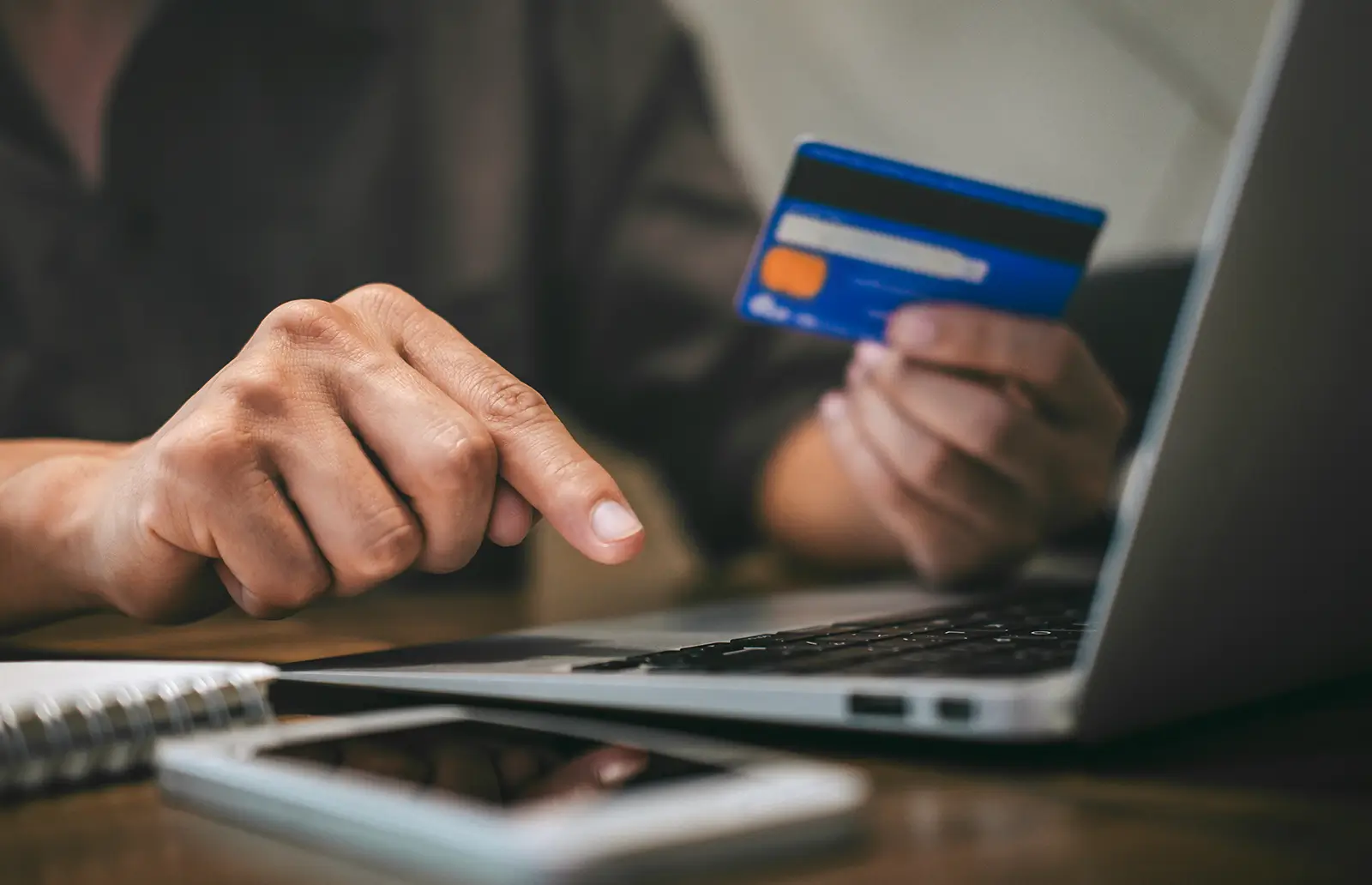 Person holding a credit card while typing on a laptop with a mobile device nearby
