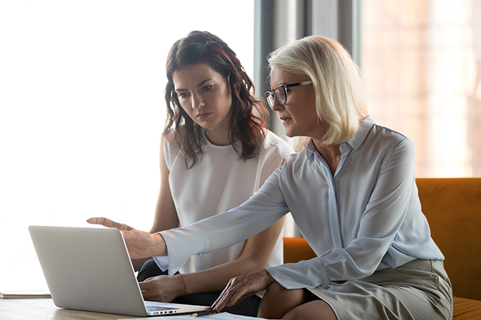 Older woman mentoring a young woman on a laptop in an office