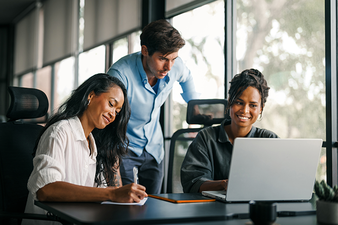 Three young professionals sitting around a laptop working together in an office