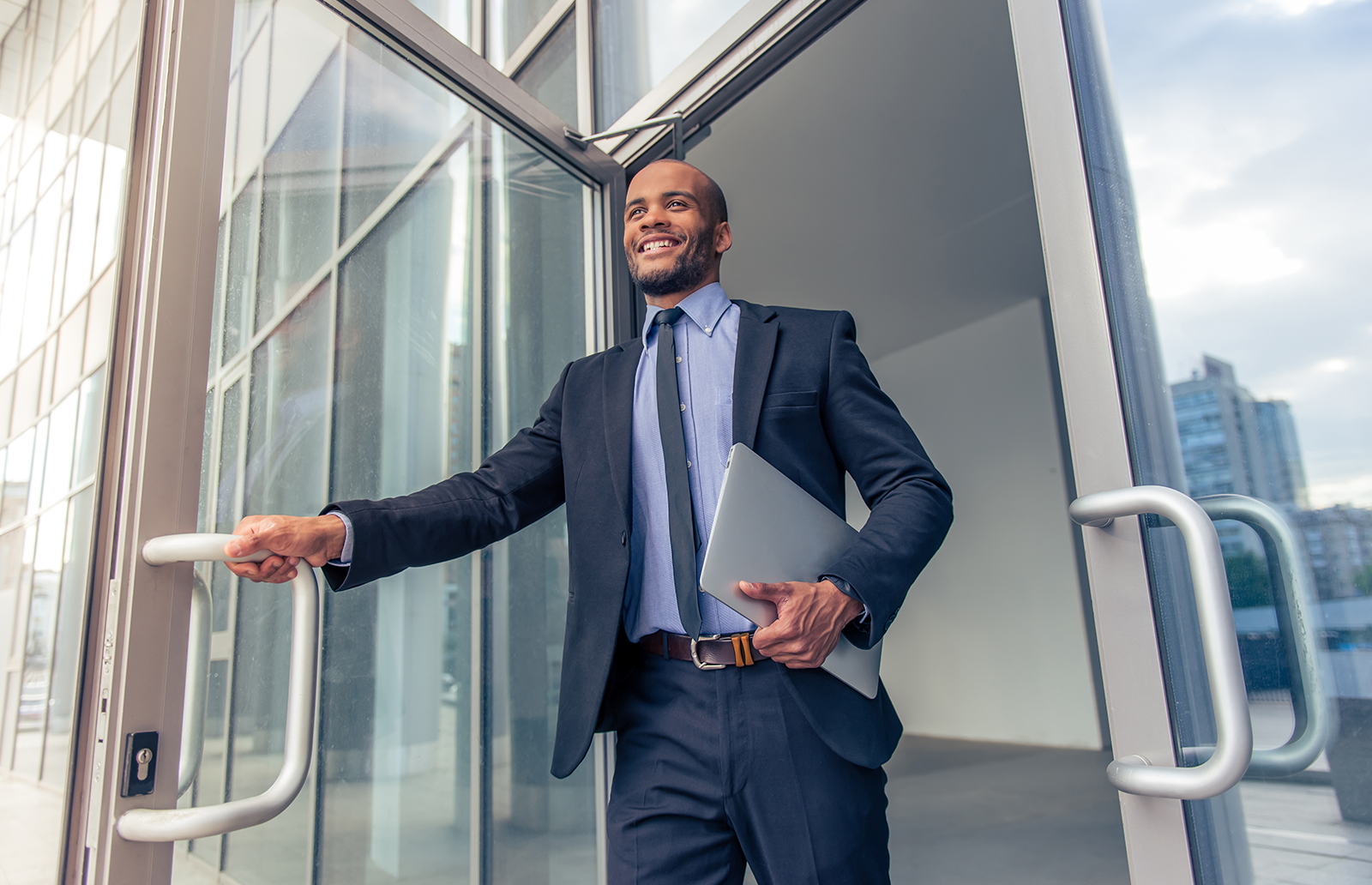 Young professional business man exiting a door with a laptop
