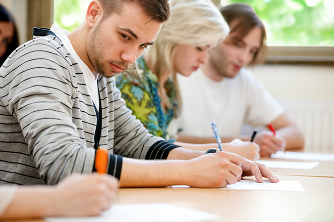 Young man sitting in a classroom taking a test and peeking at someone else's answers
