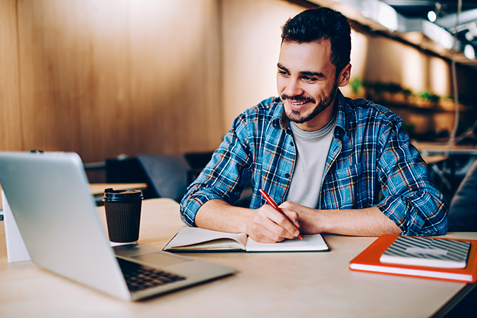 Young man sitting in front of a laptop taking notes in a classroom