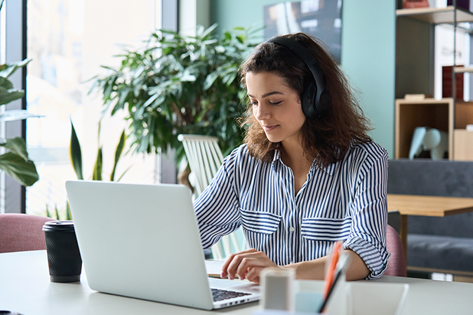 Young woman wearing headphones while working her laptop