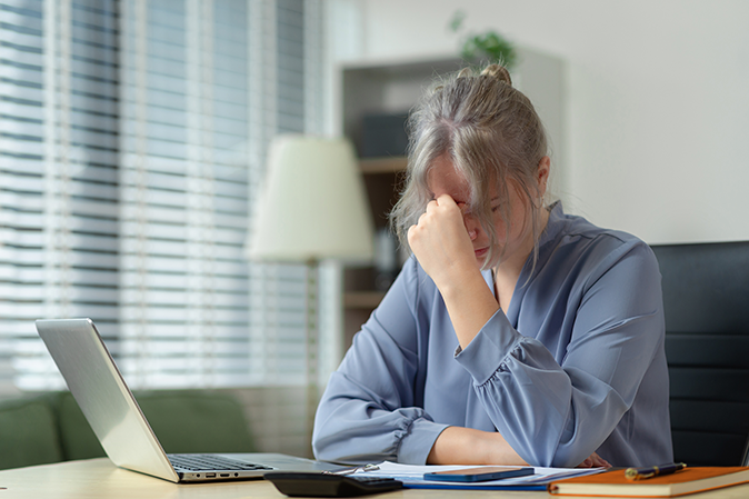 Young professional woman sitting in front of a laptop with hand on forehead in failure