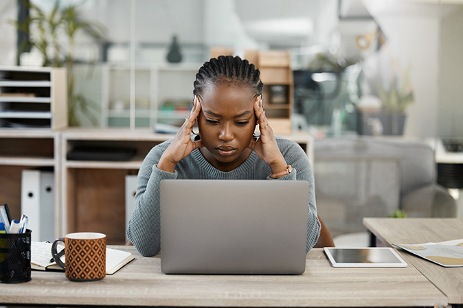 Young woman holding their head in defeat in front of a laptop and tablet