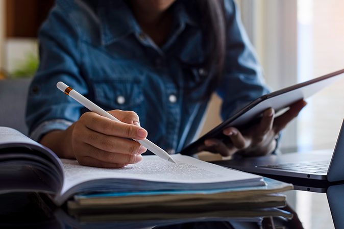 Young woman holding a tablet and using a pen to follow along in a textbook